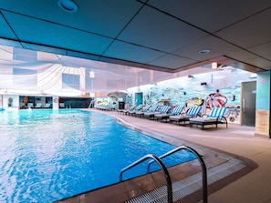 Une piscine intérieure dotée de chaises longues et ornée d’une fresque murale.