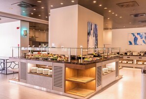 Un buffet moderne, avec un espace central de service, plusieurs stations de restauration et une rambarde en verre.