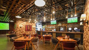 Un ristorante con tavoli e sedie in legno, un'area bar e uno schermo che mostra una partita sportiva.