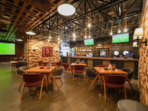 En restaurant med træborde og stole, et barområde og et skærm, der viser en sportsbegivenhed.