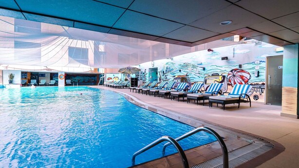 En indendørs swimmingpool med liggestole og et vægmaleri.
