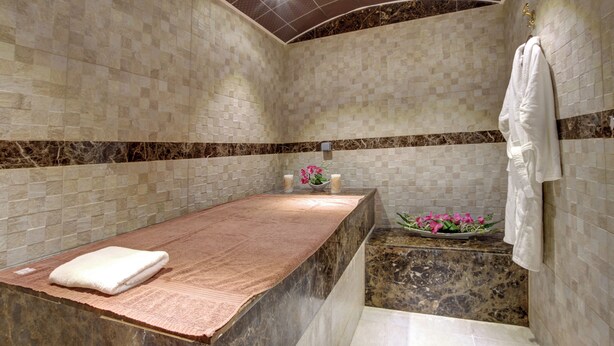 Ein Spa-Raum mit Marmorplatte, einem Handtuch, einer Blumenkomposition und einer Duschkabine.