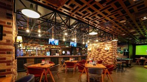 Eine Bar mit mehreren Fernsehern, Holztischen und roten Stühlen.