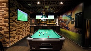 A pool table in a bar area with brick walls and multiple screens displaying sports. - Mercure BH | 1BR Sky Apt | Spacious Living on Sheikh Zayed Rd | 2 Units (Dubai)