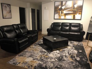 A living room with two black leather sofas, a black coffee table, and a patterned rug. - 2-bedroom apartment in tranquil Birmingham with AC for relaxing stays (Birmingham)