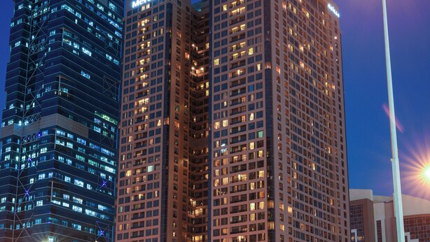 Een hoog gebouw met verlichte reclameborden, een modern architectonisch ontwerp en een uitzicht over het omliggende stadslandschap.