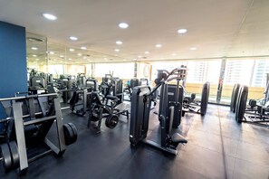 Et fitnessrum med forskellige træningsmaskiner, en spejlvæg og store vinduer.