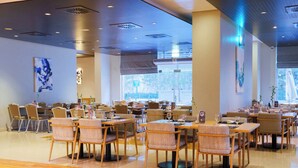 A spacious dining area with multiple tables and chairs, large windows, and ceiling lights.