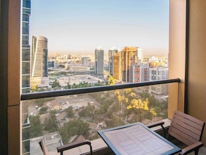 A balcony with a table and chairs, overlooking a cityscape with high-rise buildings. - 1BR City Apt | Mercure BH | Metro Facing, Pool, Kids Club (Dubai)