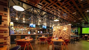 A bar area with multiple TVs, wooden tables, and red chairs.