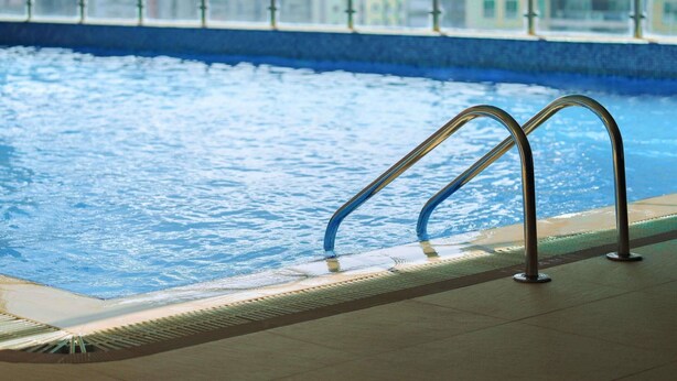 An indoor swimming pool with metal railings and a tiled floor.