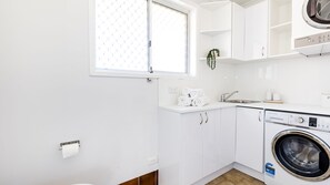 Cocina compacta con lavadora, un lavamanos y una ventana con diseño de cuadrícula blanca.