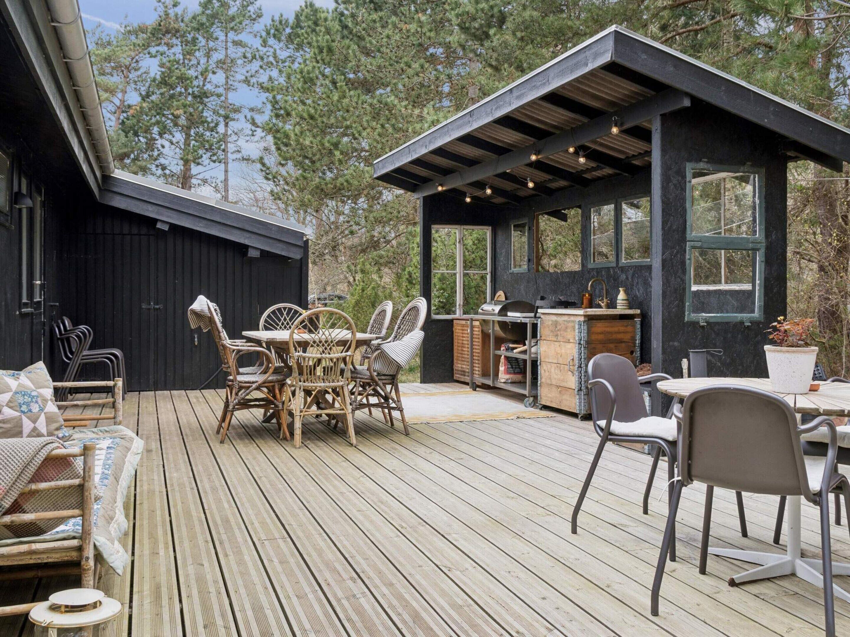 A wooden deck with outdoor furniture, a barbecue area, and a small building with windows.