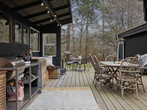 An outdoor deck with a grill, dining table, chairs, and a view of trees. - 4 Star Holiday Home in Hojby (Hojby)