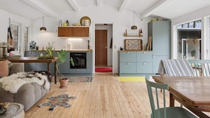 Ein geräumiges Wohnzimmer mit Holzboden, einer Couch, einem Esstisch und einer Küchenzeile mit Holzausbau und einem Einbauofen.