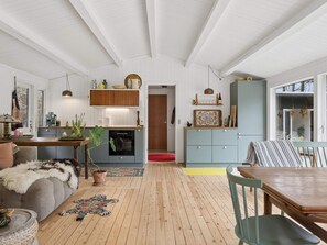 Ein geräumiges Wohnzimmer mit Holzboden, einer Couch, einem Esstisch und einer Küchenzeile mit Holzausbau und einem Einbauofen.