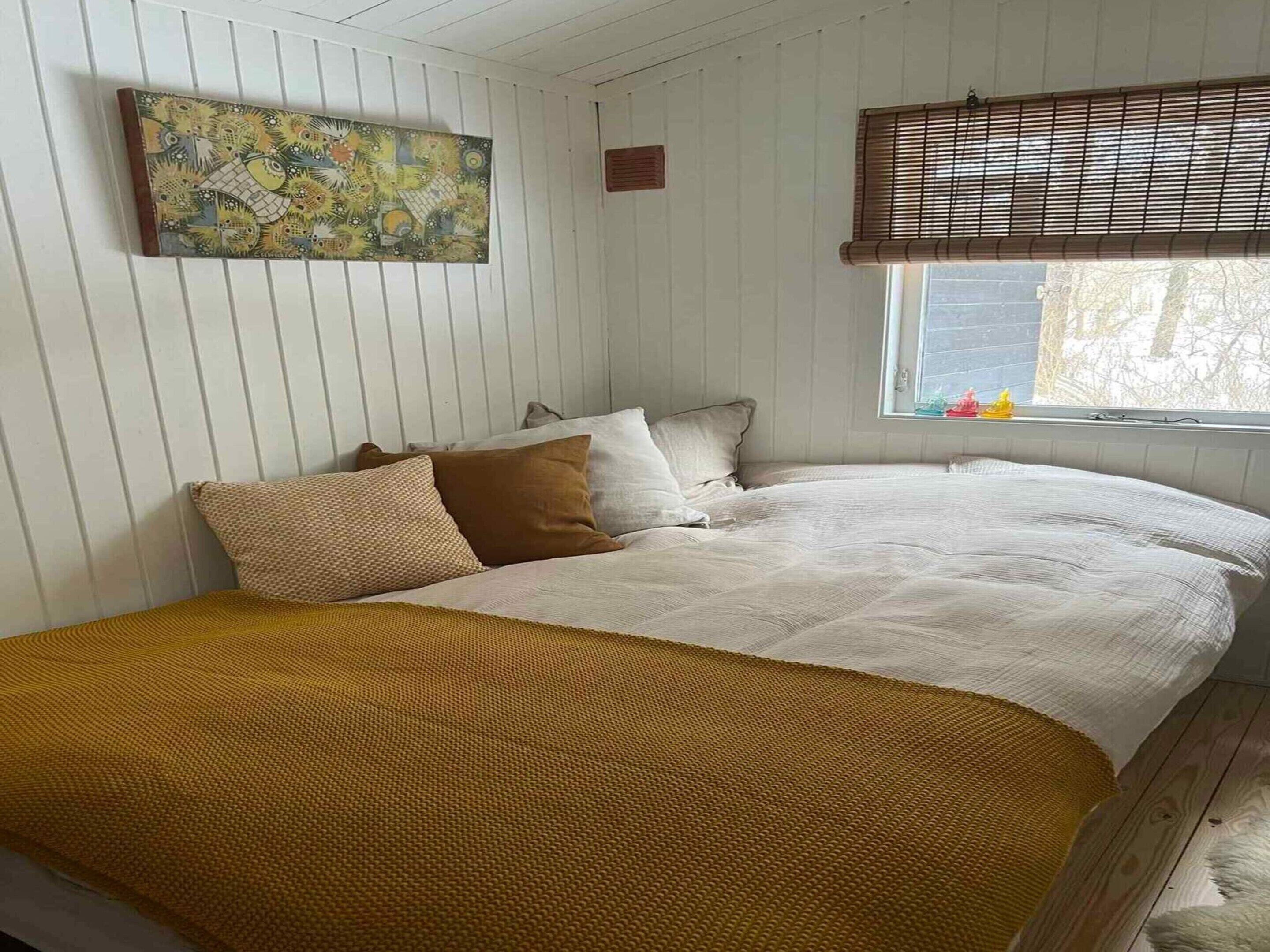 A bedroom with a bed, pillows, a blanket, a window with blinds, and a wall-mounted painting.