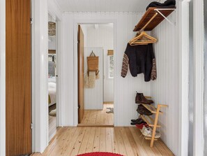 Ein Flur mit Holzboden, einem roten Teppich, einem Schuhregal und einem Kleiderständer mit Pullover und Jacke.
