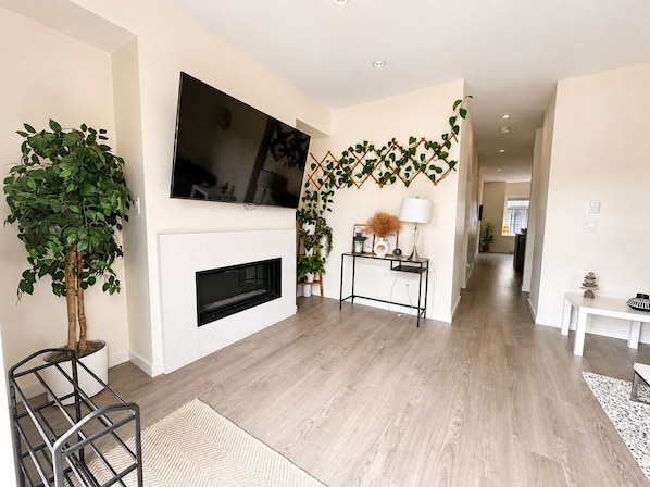 A modern living room with a flat-screen TV, fireplace, and potted plants.