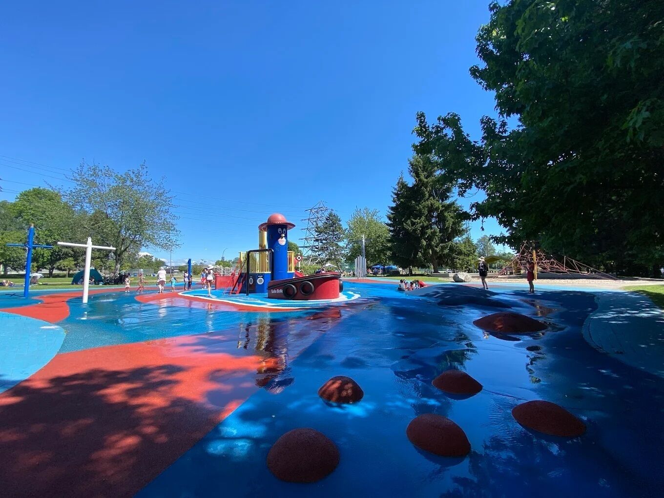 Parque acuático con una zona de juegos azul y roja, un tobogán de agua y un árbol grande.