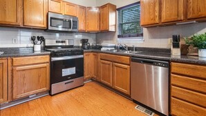Una cocina con armarios de madera, electrodomésticos de acero inoxidable y un ventanal con persianas.