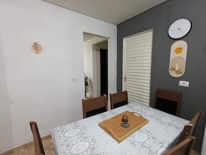 Zona de dinar amb una taula preparada per a dues persones, cadires, un rellotge i una porta.