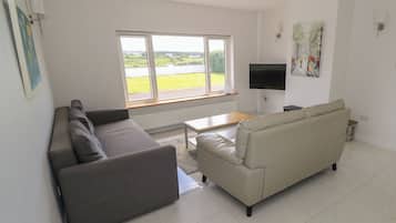 A modern living room with a grey sofa, a beige sofa, a coffee table, and a TV mounted on the wall.