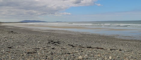 A pebbly beach with distant mountains and a cloudy sky.