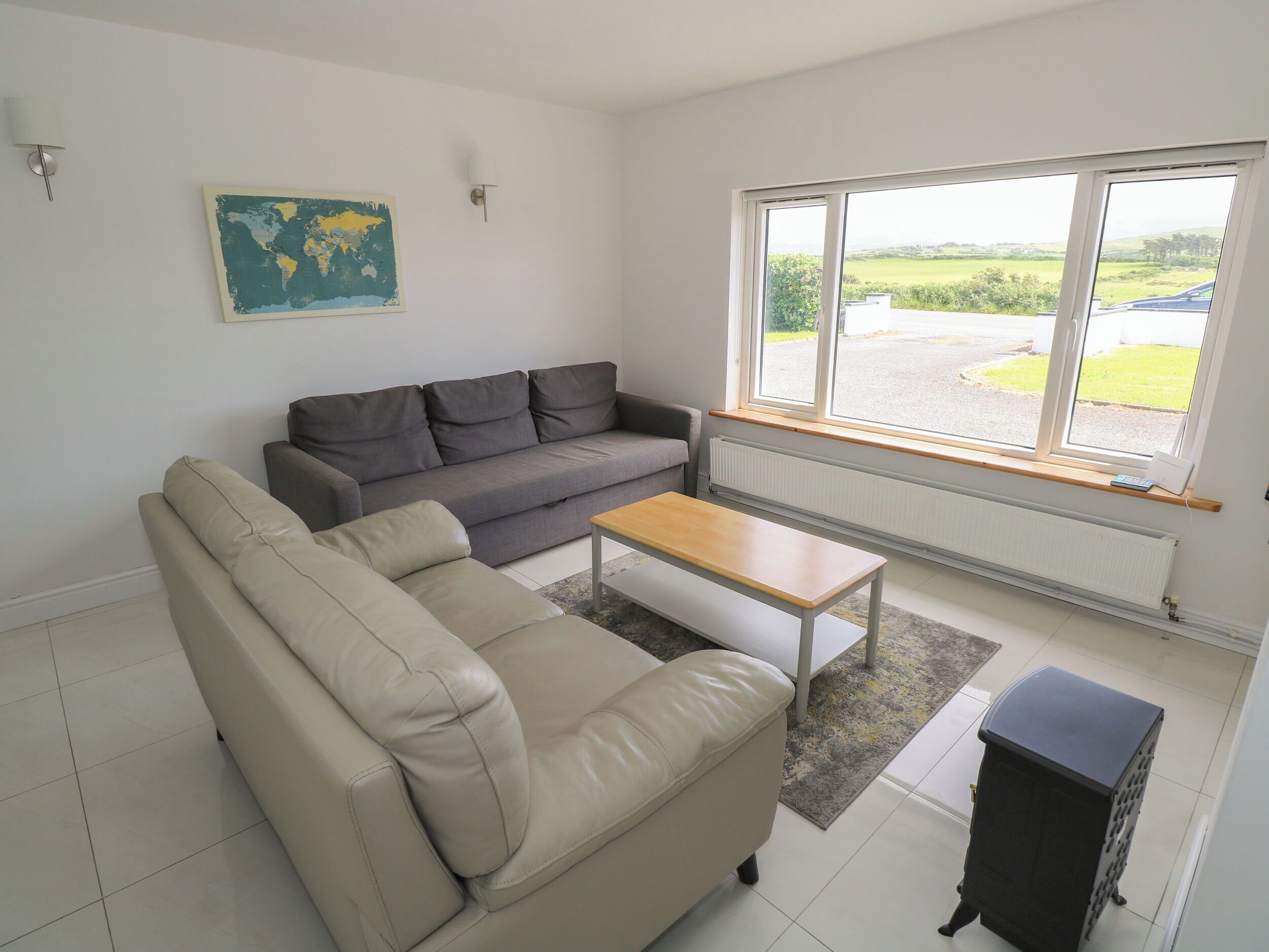 A living room with a grey sofa, a beige sofa, a wooden coffee table, a black cabinet, and a large window with a view of greenery.