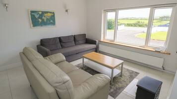 A living room with a grey sofa, a beige sofa, a wooden coffee table, a black cabinet, and a large window with a view of greenery.