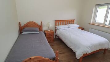 A room with two wooden beds, a nightstand with a lamp, a window, and a radiator.