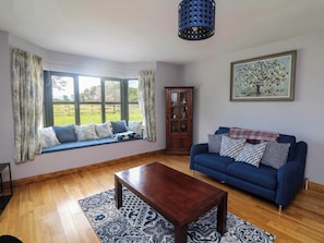 Un salon avec un canapé bleu, une table basse en bois, un banc de fenêtre agrémenté de coussins, un meuble et un tableau accroché au mur.