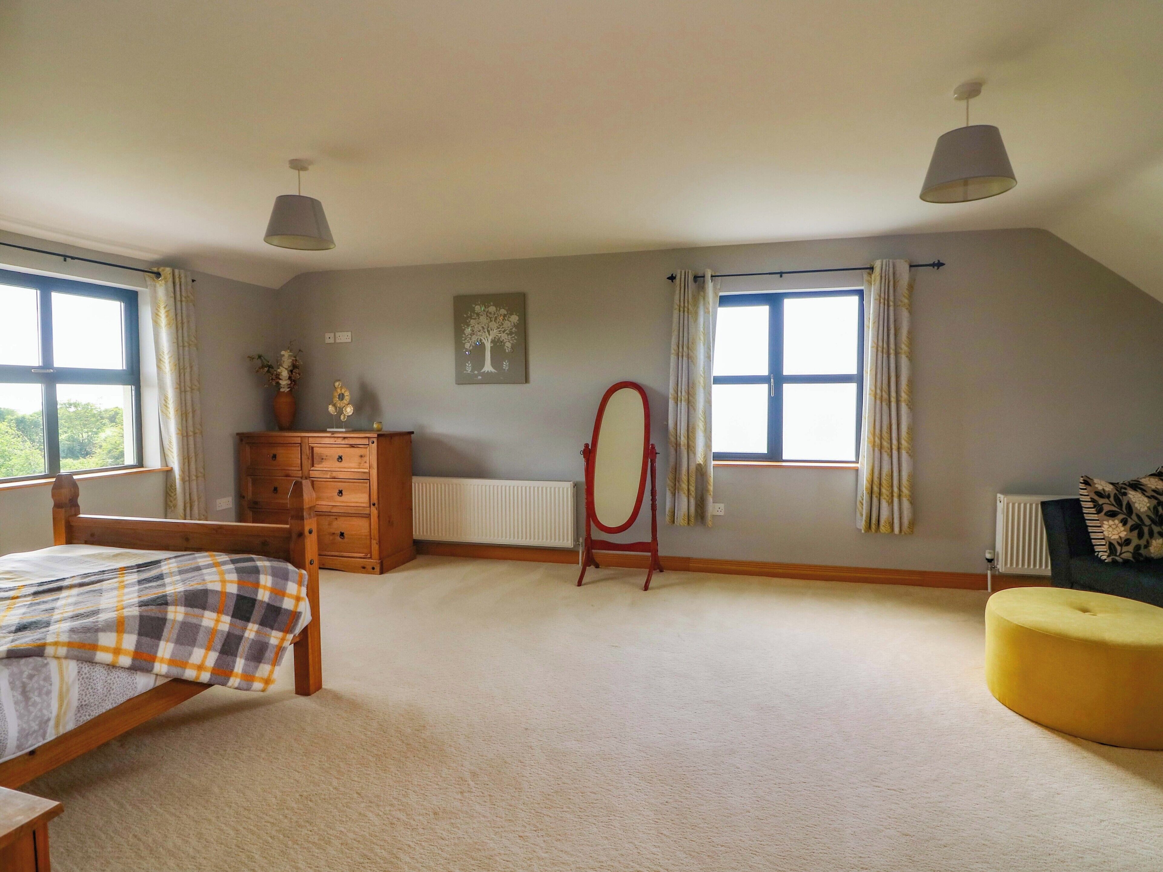 Ein Schlafzimmer mit Bett, Schminktisch, Kommode und einem Fenster mit Vorhängen.
