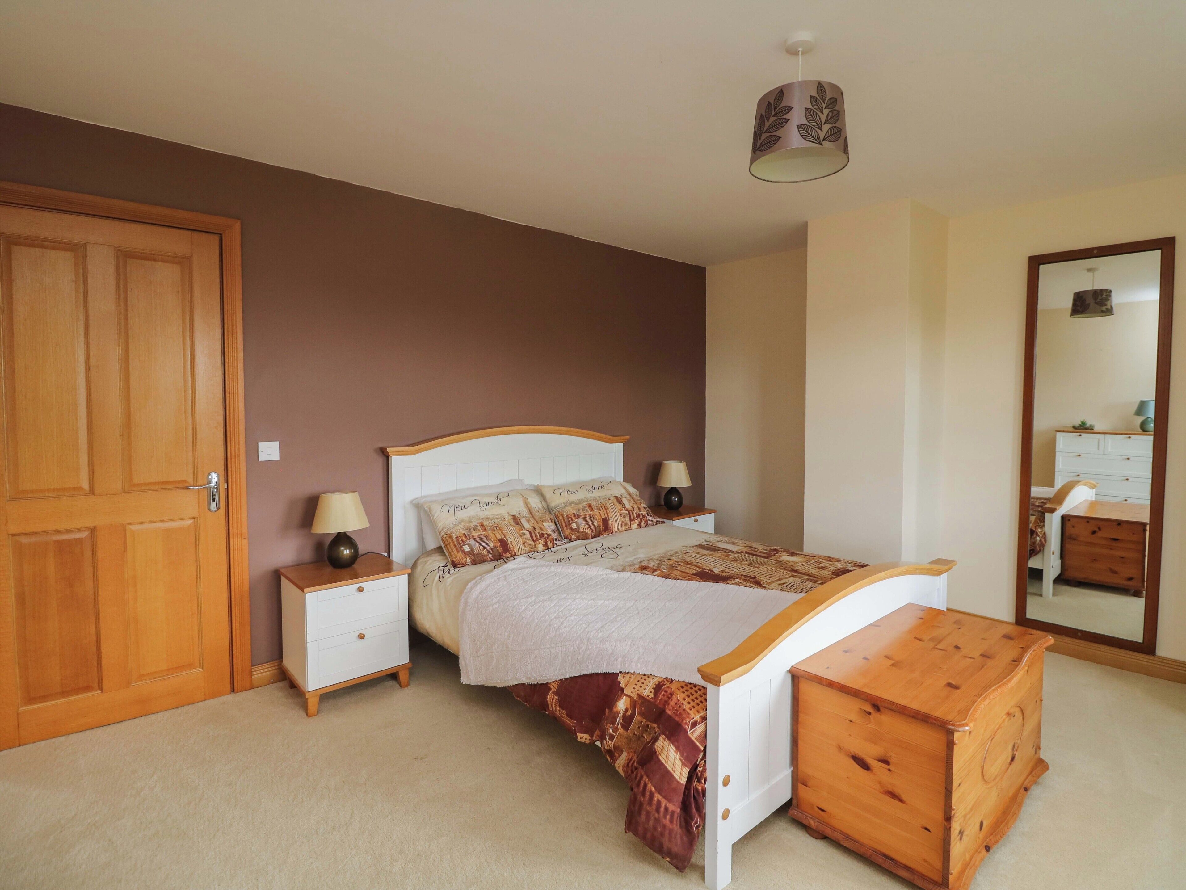 A bedroom with a bed, bedside tables, a wooden chest, a wardrobe, and a mirror.