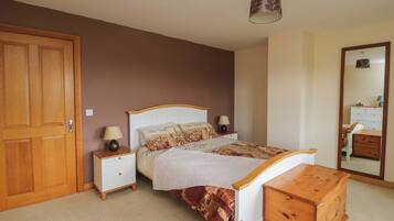 A bedroom with a bed, bedside tables, a wooden chest, a wardrobe, and a mirror.