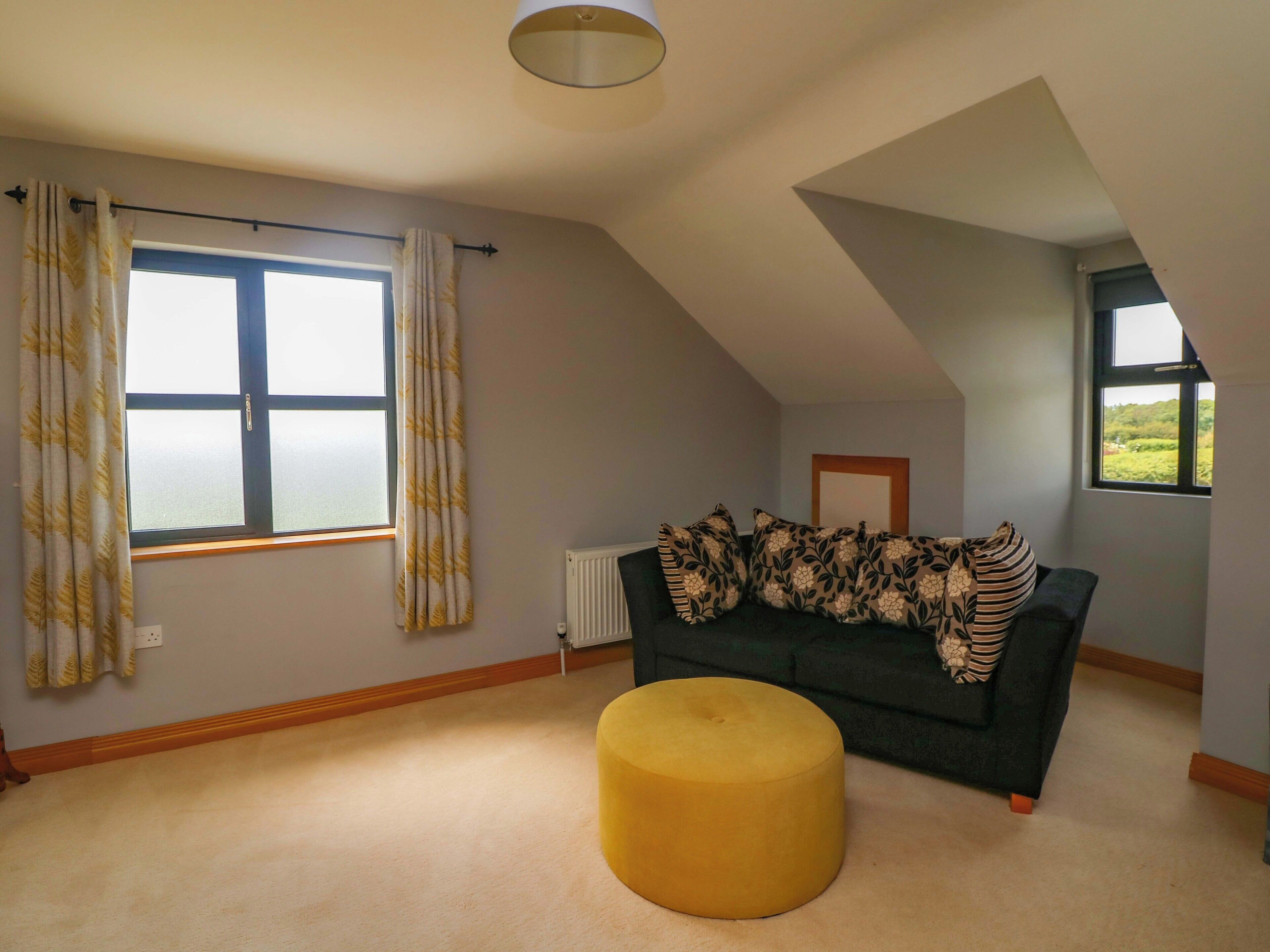 A room with a large window, a radiator, a dark sofa, and a yellow ottoman.