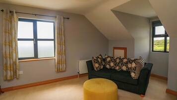 A room with a large window, a radiator, a dark sofa, and a yellow ottoman.