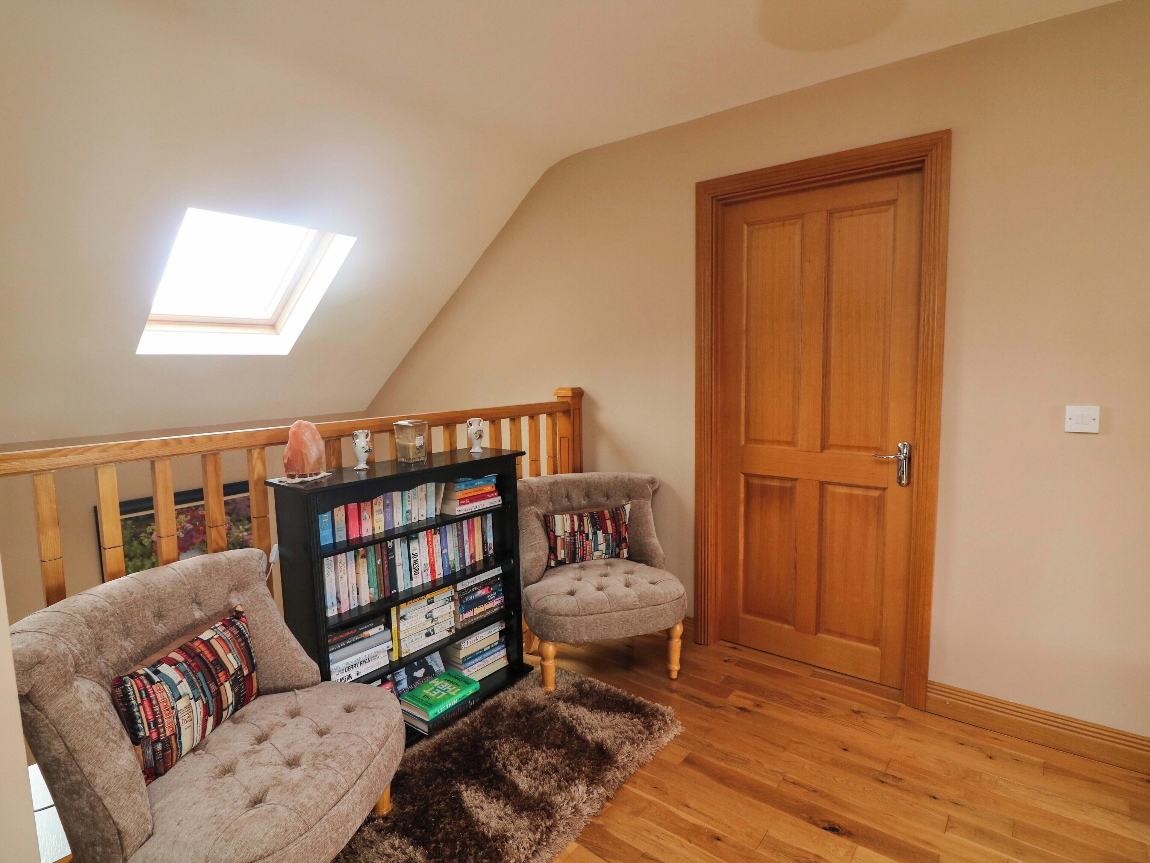 Ein Schlafzimmer im Loft-Stil mit schrägem Dach, einer Holztür, einem Bücherregal, zwei Sesseln und einem flauschigen Teppich.