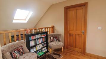 Ein Schlafzimmer im Loft-Stil mit schrägem Dach, einer Holztür, einem Bücherregal, zwei Sesseln und einem flauschigen Teppich.