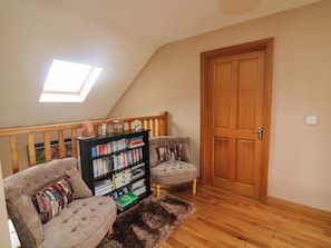 Ein Schlafzimmer im Loft-Stil mit schrägem Dach, einer Holztür, einem Bücherregal, zwei Sesseln und einem flauschigen Teppich.