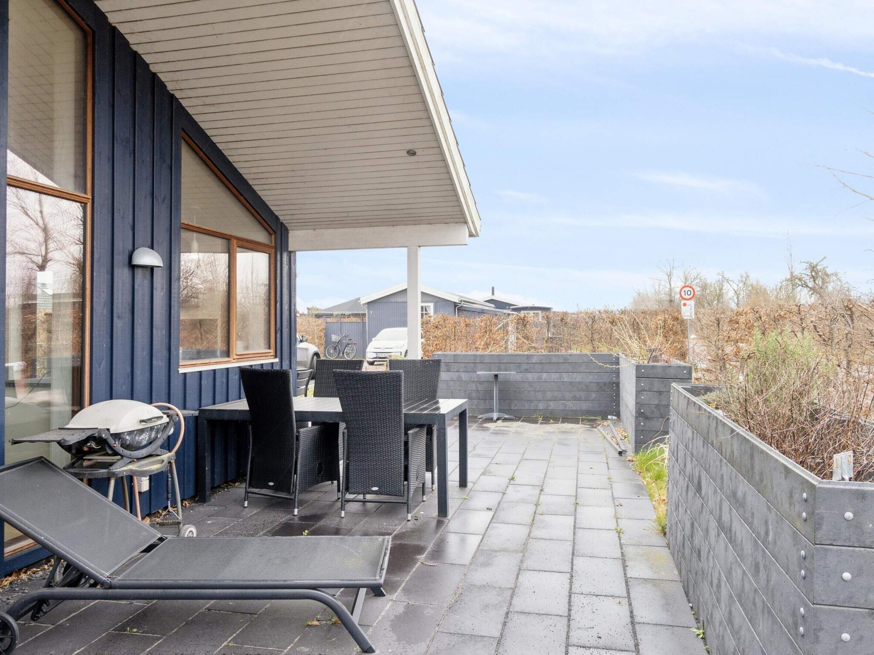 A covered outdoor patio with seating, a grill, and a paved walkway.