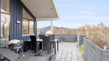A covered outdoor patio with seating, a grill, and a paved walkway.