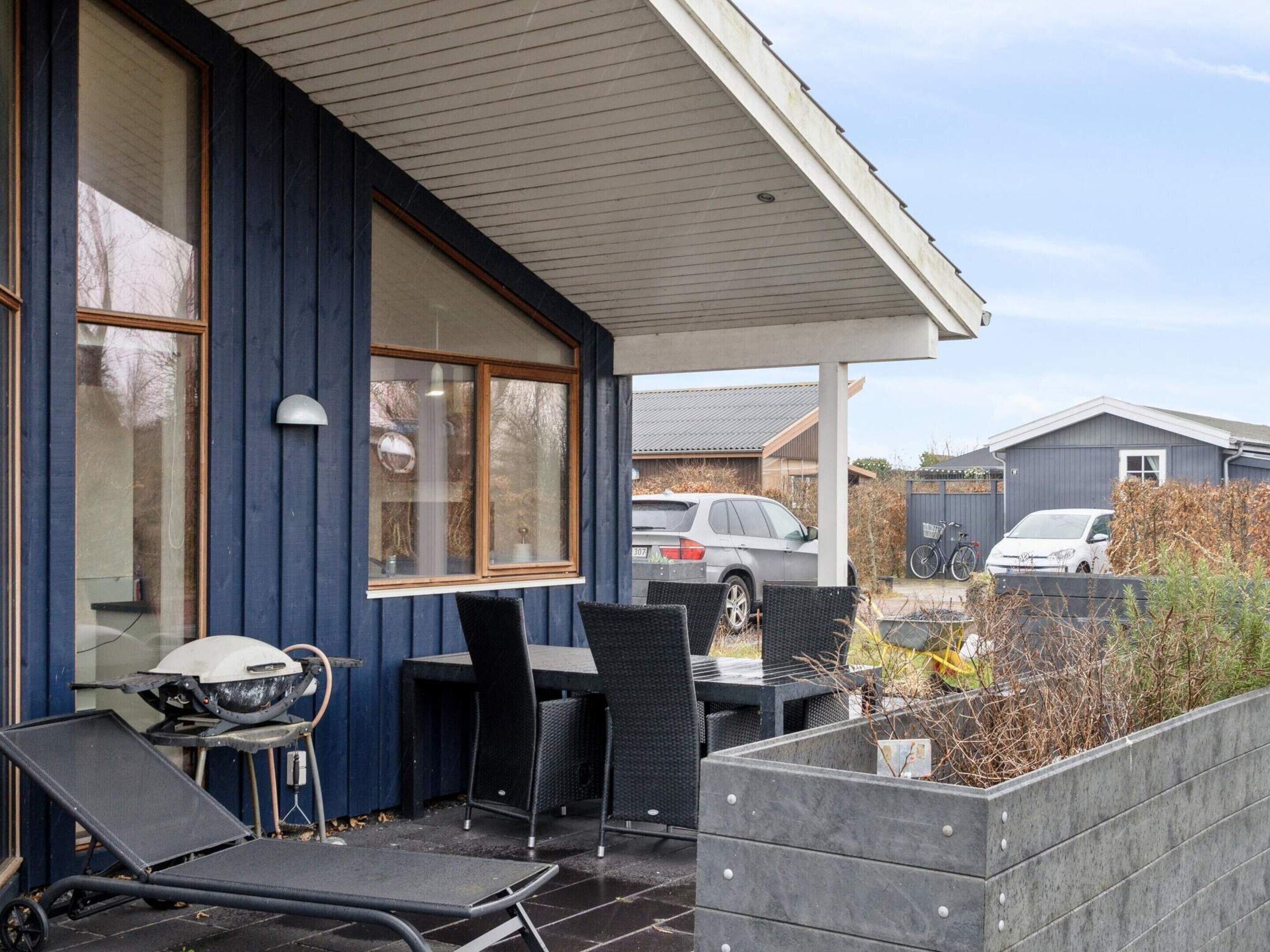 A covered outdoor area with a table and chairs, a grill, and a car parked in the background.