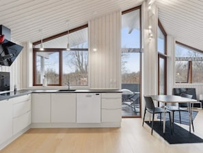 Une cuisine moderne dotée d’un grand îlot central, d’un coin repas avec une table et des chaises, et de grandes fenêtres offrant une vue sur l’extérieur.