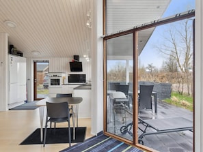 Une cuisine moderne avec des meubles blancs, un coin repas avec une table et des chaises, et une grande porte-fenêtre coulissante donnant sur un patio extérieur aménagé avec des sièges.