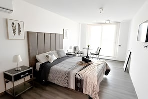 A modern bedroom with a large bed, bedside tables, a desk, a chair, and a window. - Depto. moderno con aire acondicionado (Santiago)