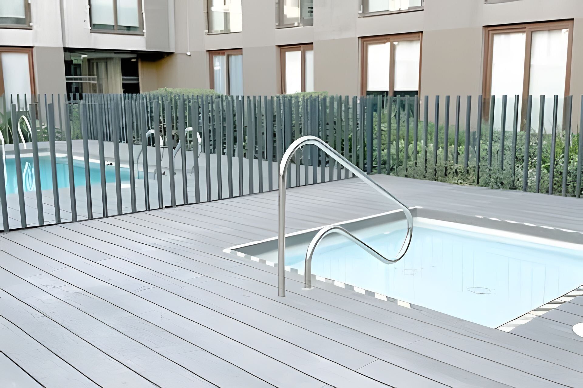 A swimming pool with a metal ladder, surrounded by a wooden deck and a metal fence.