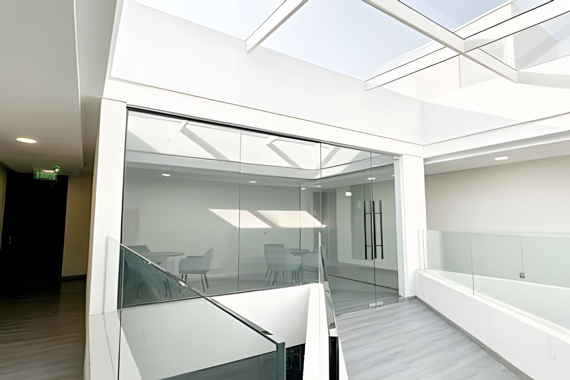 A modern interior with a glass-walled meeting room, a staircase, and a high ceiling with skylights.