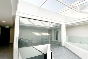 A modern interior with a glass-walled meeting room, a staircase, and a high ceiling with skylights. - Depto. moderno con aire acondicionado (Santiago)