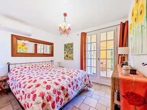 A bedroom with a bed, a chandelier, a mirror, a door leading to a balcony, and a painting on the wall. - Villa Vivaris (VEN111) by Interhome (Vence)